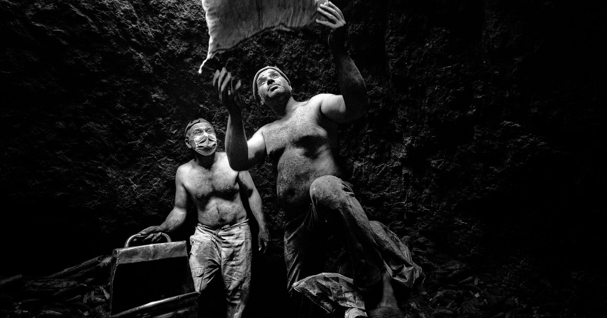 Two shirtless coal miners work together underground, emphasizing teamwork and labor.