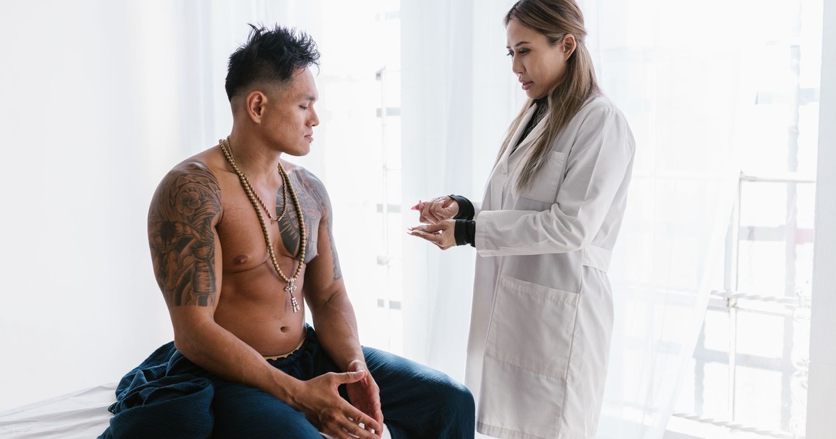 A doctor consults with a shirtless man in a clinical setting. Healthcare interaction.