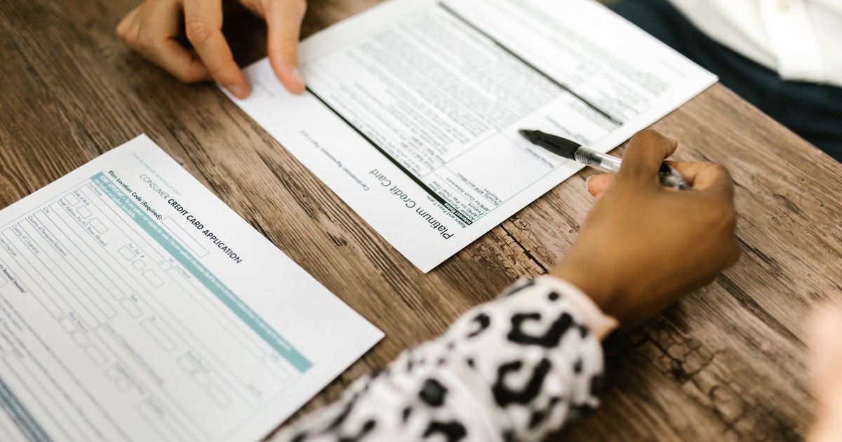 Close-up of two people reviewing and filling out a credit card application on a wooden table.
