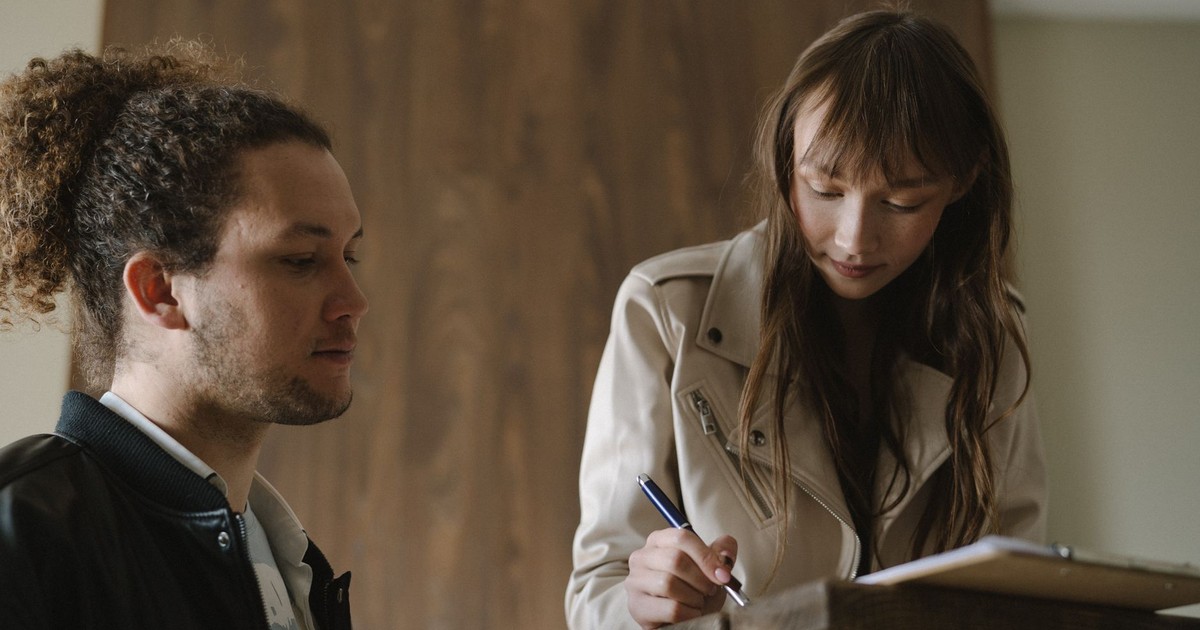A young couple reviews and signs real estate documents indoors.