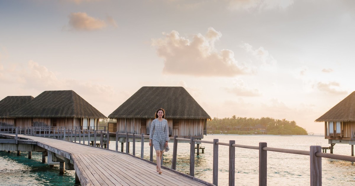 A woman strolling along a boardwalk in the Maldives during a tranquil dusk with overwater bungalows in the background.