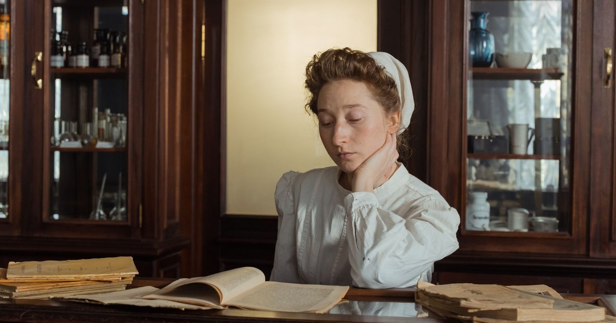 A female pharmacist in vintage attire reads in an old apothecary shop.