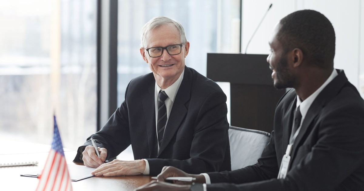 Two business professionals discussing and signing documents at a meeting with an American flag on the table.