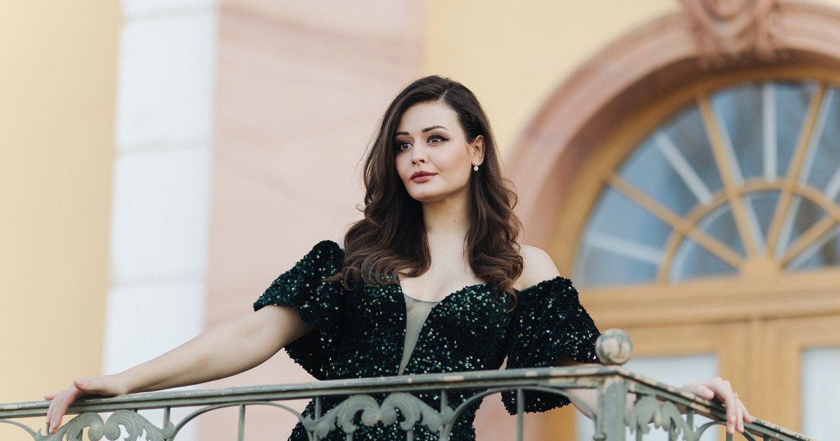 A woman in an elegant green dress stands confidently on a stylish balcony.