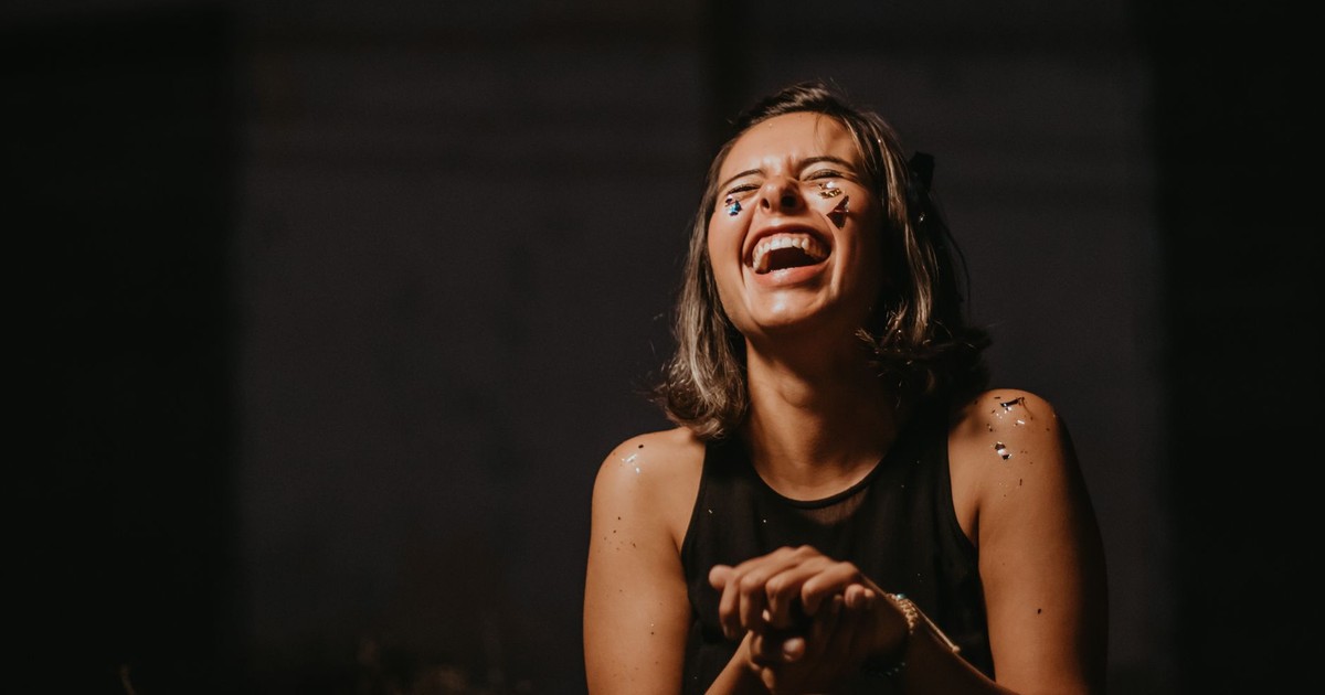 A joyful young woman laughing with confetti on a dark background.