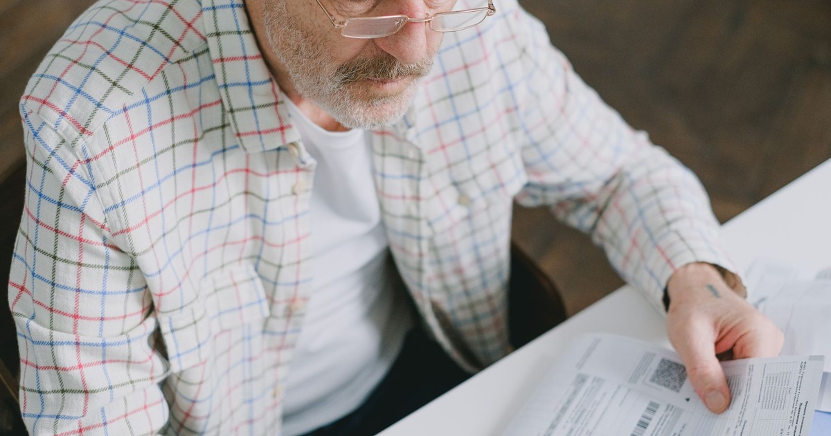 Elderly man in glasses carefully examines documents at home. Thoughtful and focused.