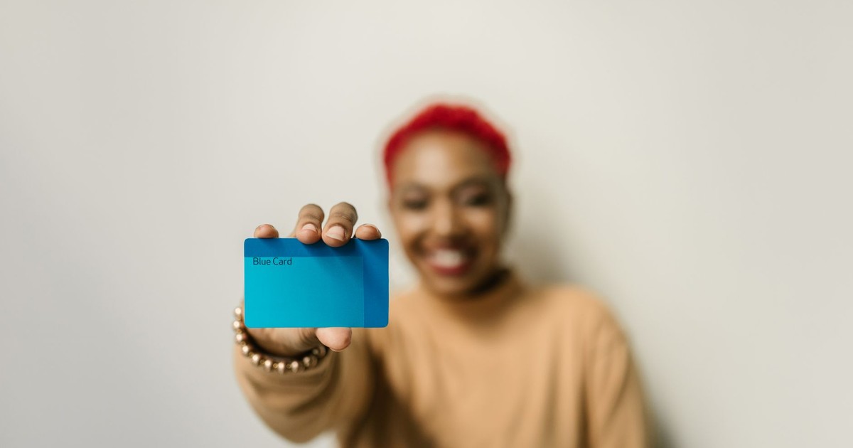 A cheerful woman with red hair displays a blue card against a neutral background, focused on the card.