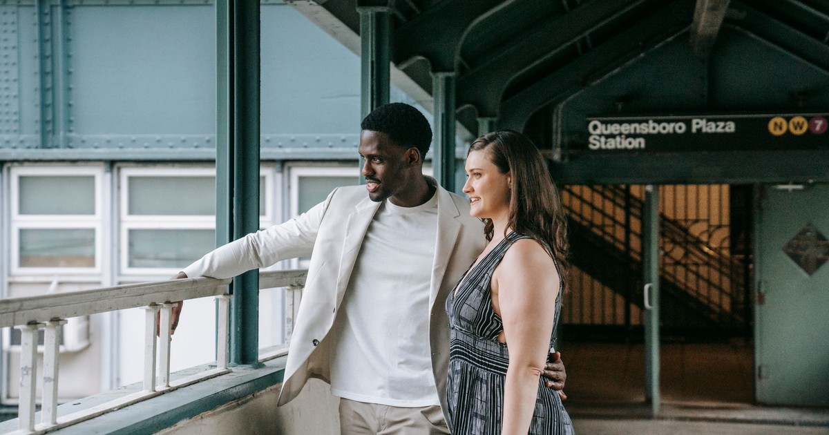 A couple lovingly embraces at Queensboro Plaza Station, capturing a candid moment of connection.