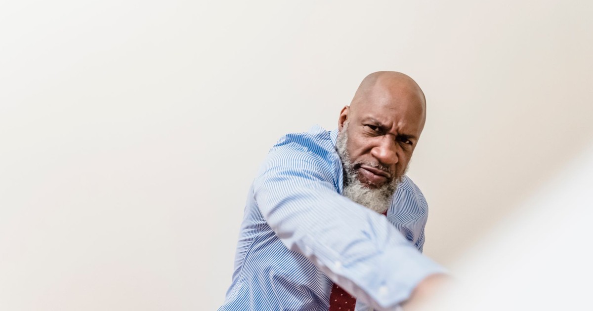 Bald bearded man in shirt displaying emotions against white background.