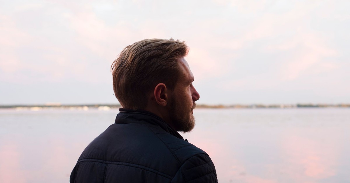 A serene side profile shot of a man gazing over a calm lake at sunset, capturing a moment of reflection.