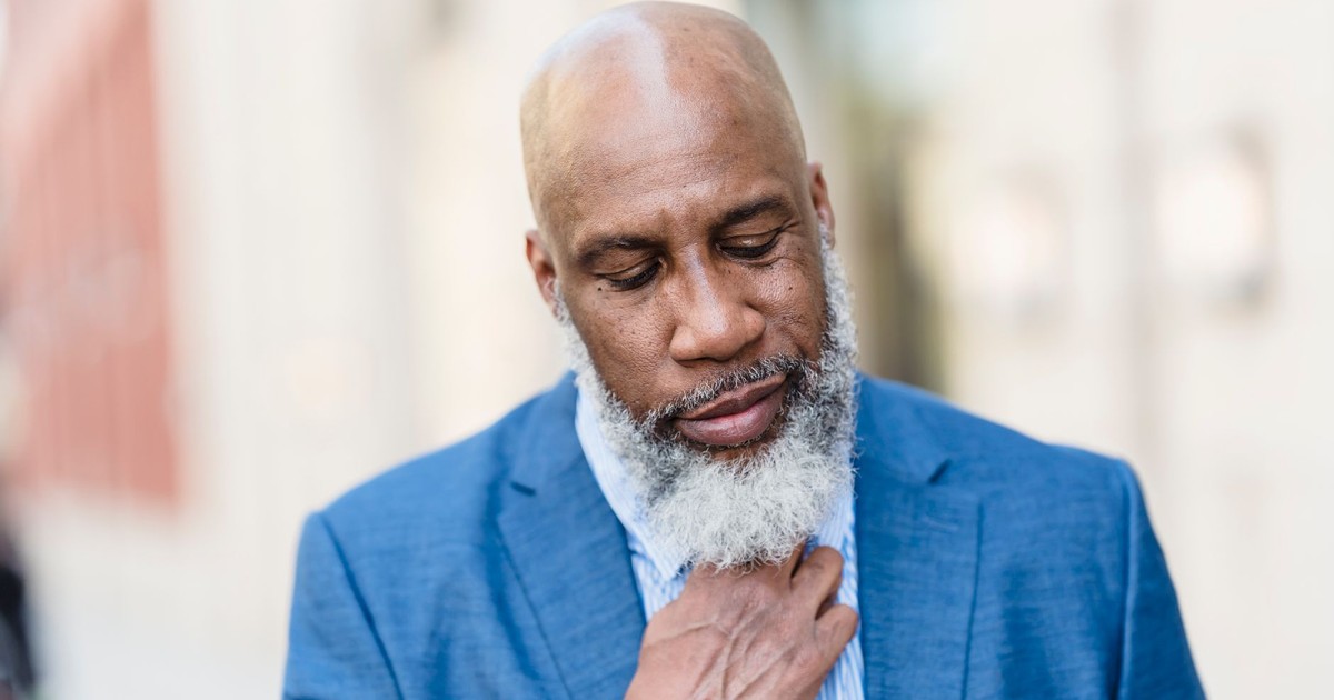 Pensive bald African American male employee with gray beard in formal outfit standing on street near building on blurred background
