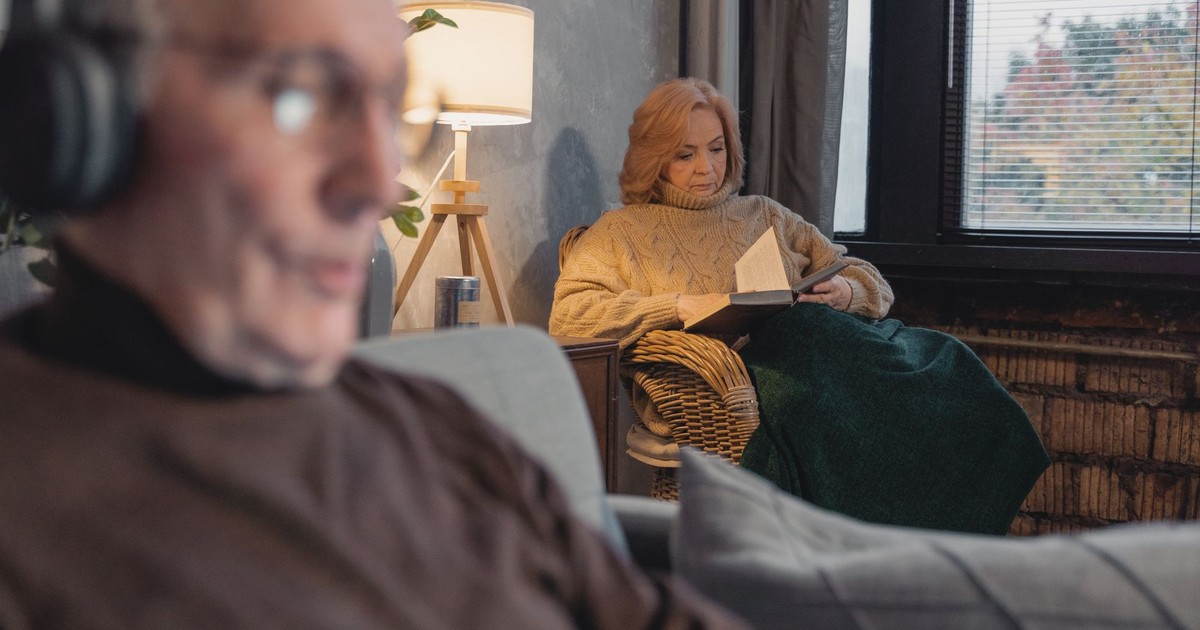 Elderly woman reading by the window, grandfather listening to music, cozy indoor setting.