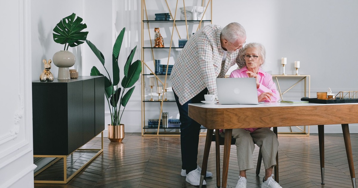 Senior couple using a laptop while discussing something in their modern living room.