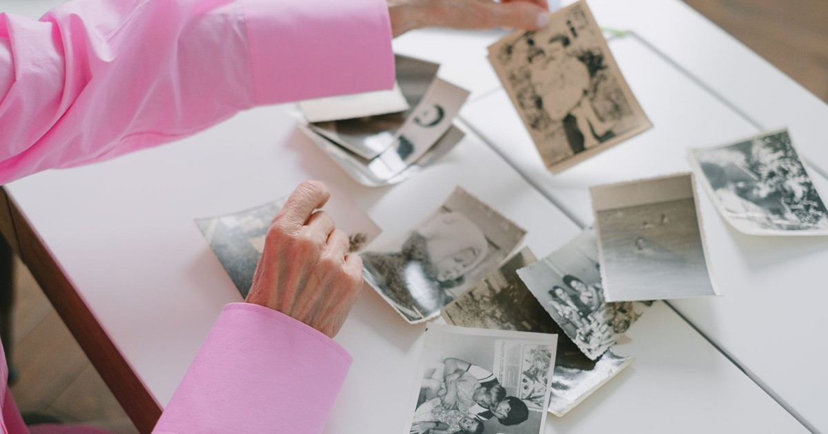 An elderly woman in a pink shirt sorting through old black and white family photographs, evoking nostalgia.