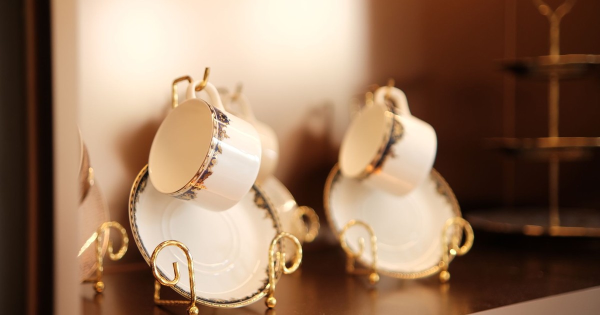 Close-up of elegant porcelain tea cups and saucers on a shelf, beautifully arranged with gold detailing.