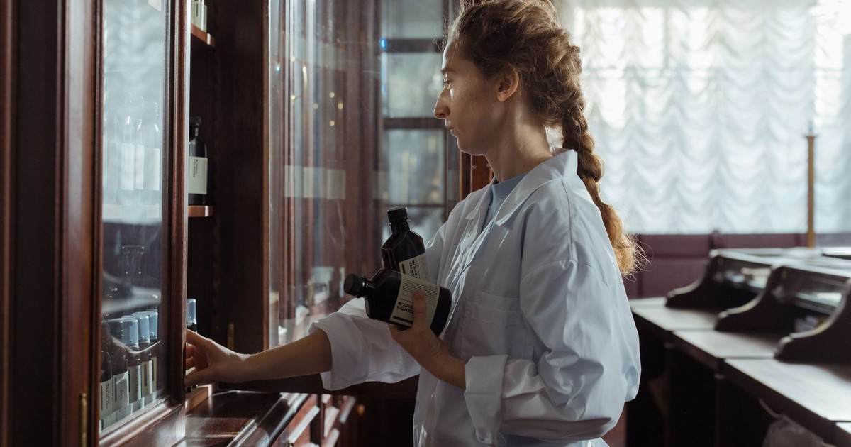 A female pharmacist arranging bottles in a classic pharmacy interior, captured indoors.