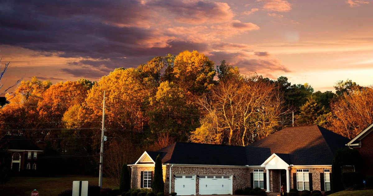 A picturesque suburban house surrounded by fall foliage under a dramatic sunset sky in Madison, AL.