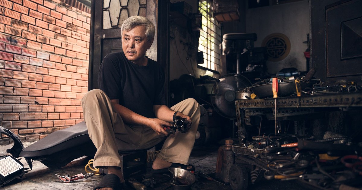 Elderly artisan in Ho Chi Minh City garage working with tools and machinery.