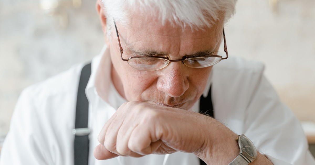 Elderly man with white hair and glasses deep in thought indoors.