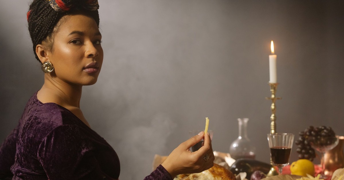 A woman enjoys a meal with wine and candlelight, featuring elegant fashion and decor.