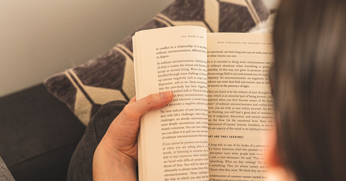 A person enjoys a relaxing reading session indoors, holding an open book on a comfy couch.