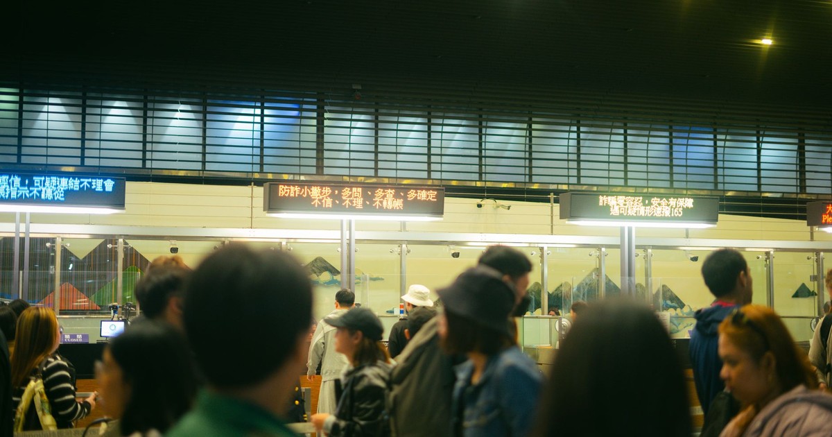 Crowded airport check-in area with people queueing and visible flight information signs.