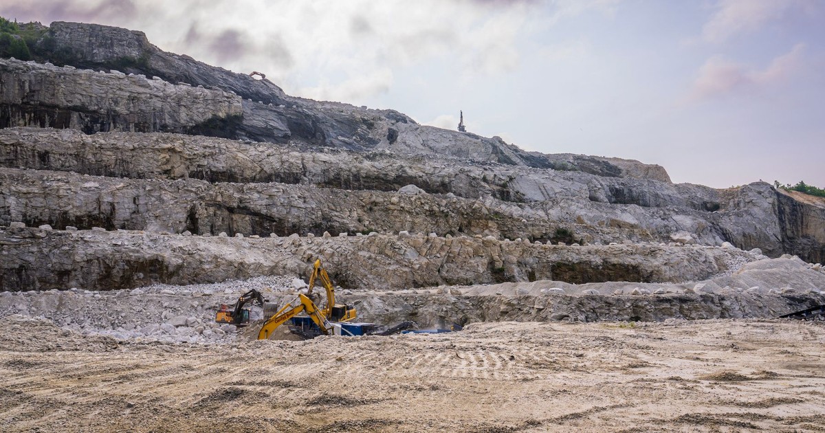 A quarry with excavators working on rocky terrain under a cloudy sky.