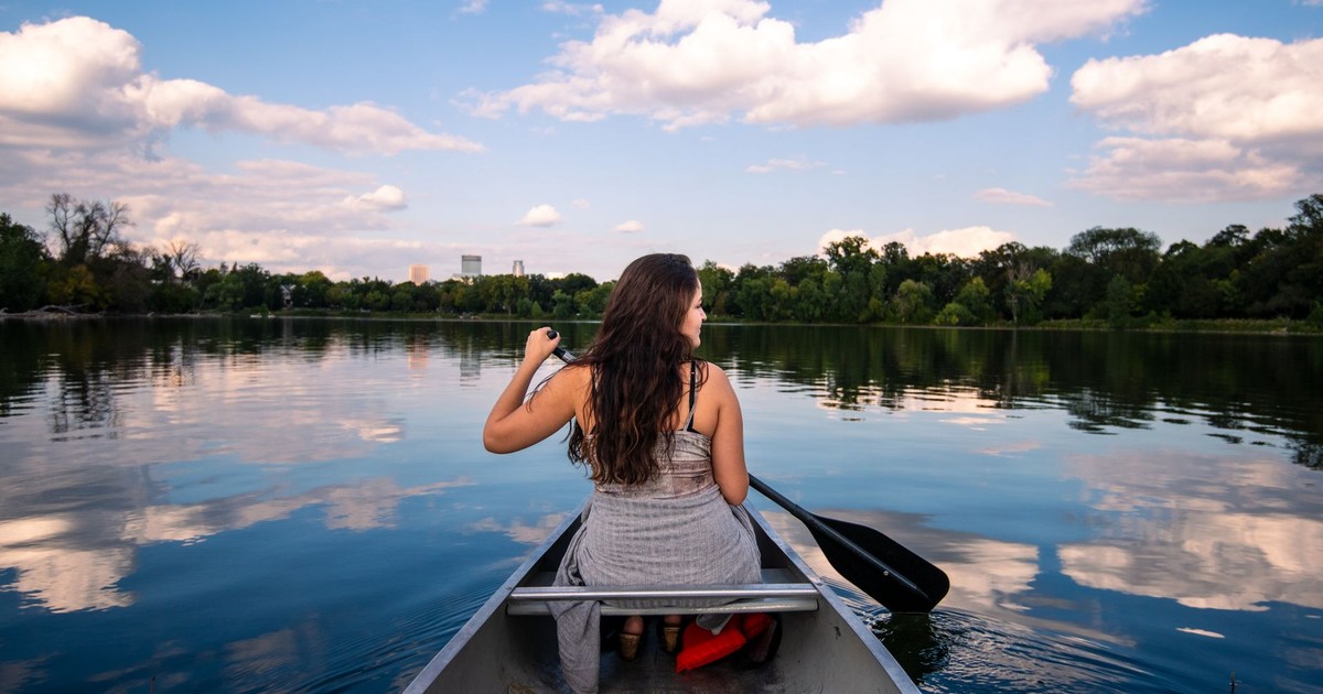 A woman canoeing on a tranquil lake in Minneapolis under a sunny sky.