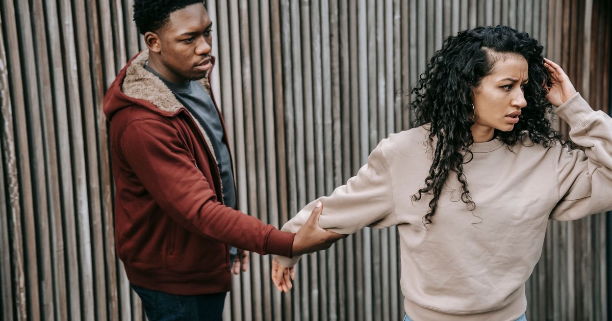 Disappointed African American male trying to stop unhappy ethnic girlfriend while having argument on street near wooden fence during breakup