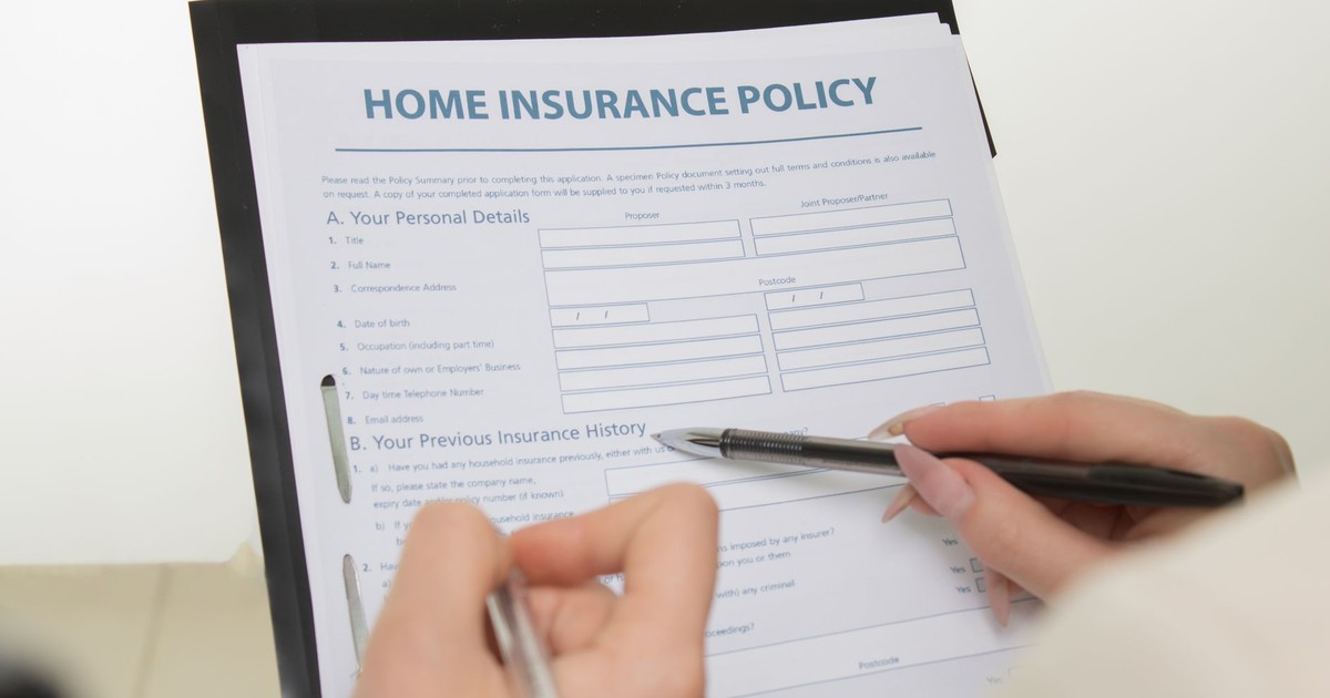 Hands holding pens filling out a home insurance policy document for coverage details.