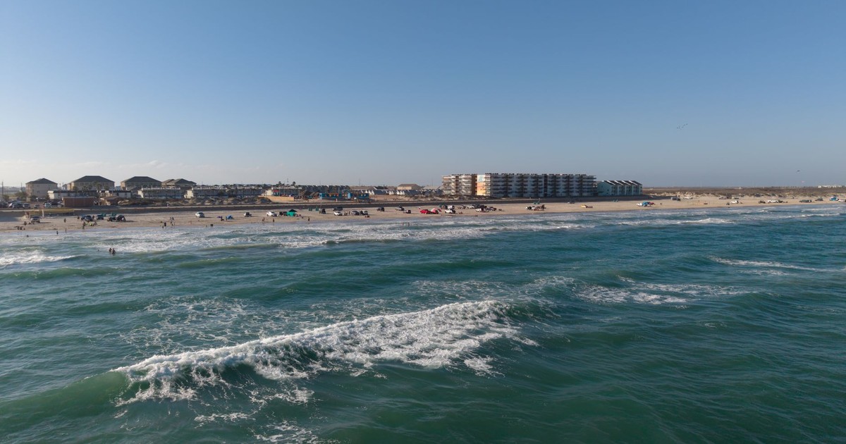 Aerial view of a sunny beach in Corpus Christi with waves and coastal buildings.