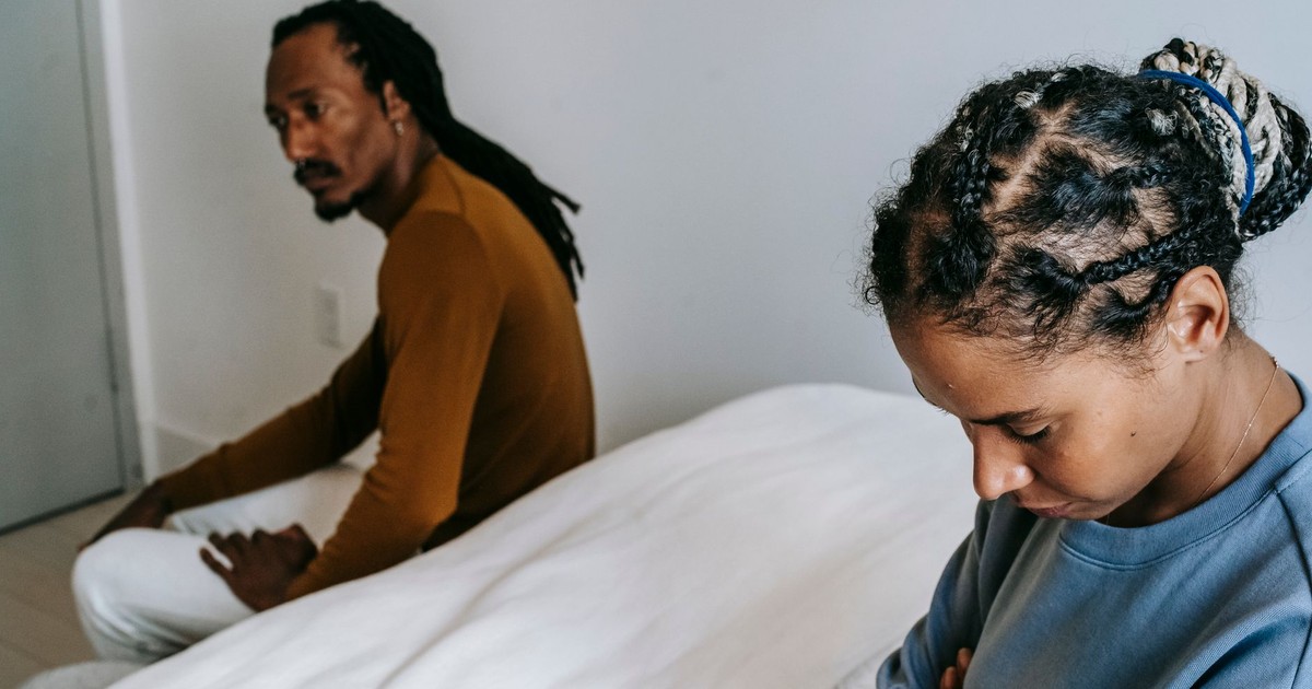 Young black couple in casual outfit sitting on bed with sad face and thinking at home