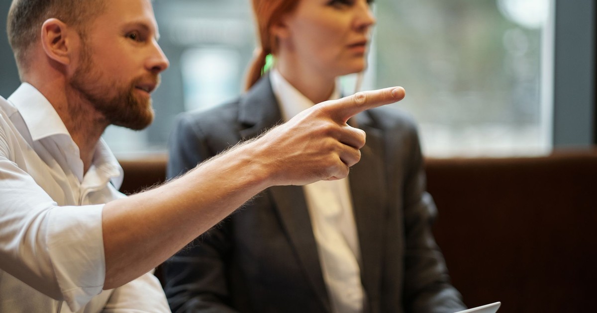 Focused business professionals in discussion, one pointing at an unseen item, captured indoors.