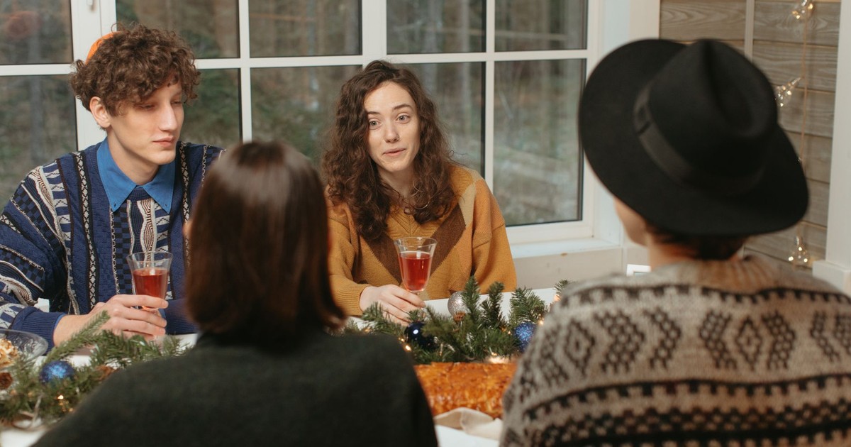 A group of friends enjoying a festive holiday meal with drinks and decorations.