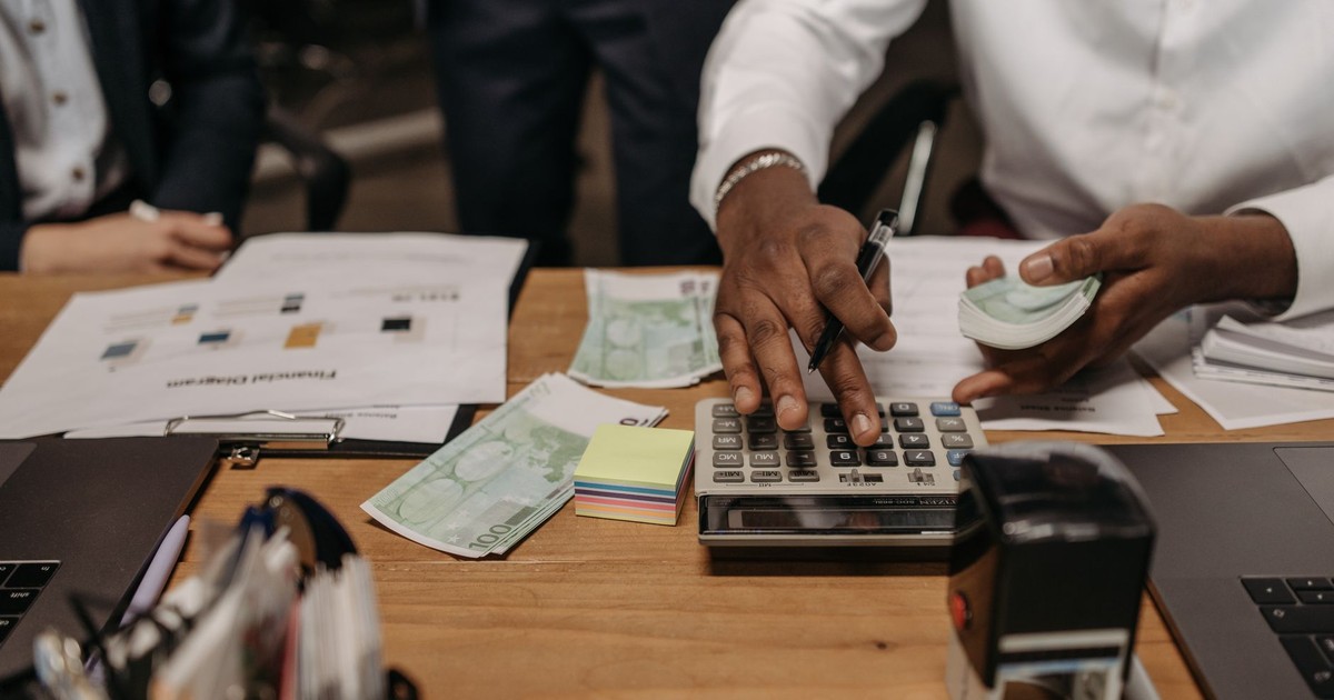 Professional setting with people handling cash and calculations using a calculator at a desk.