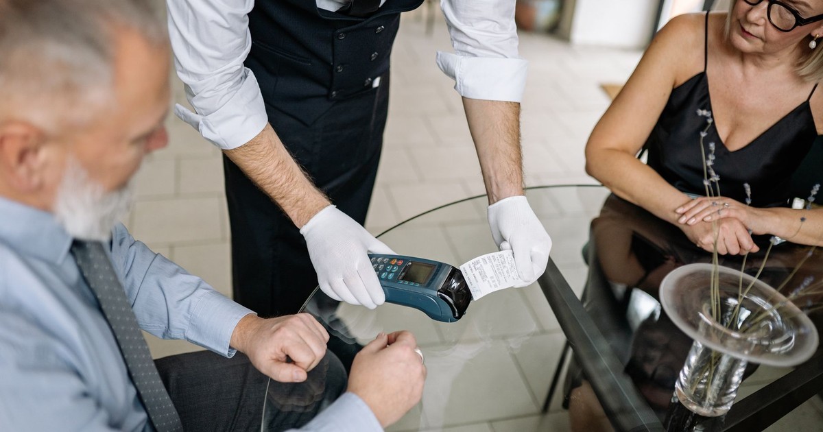 A couple making a contactless payment using a credit card at a restaurant table.