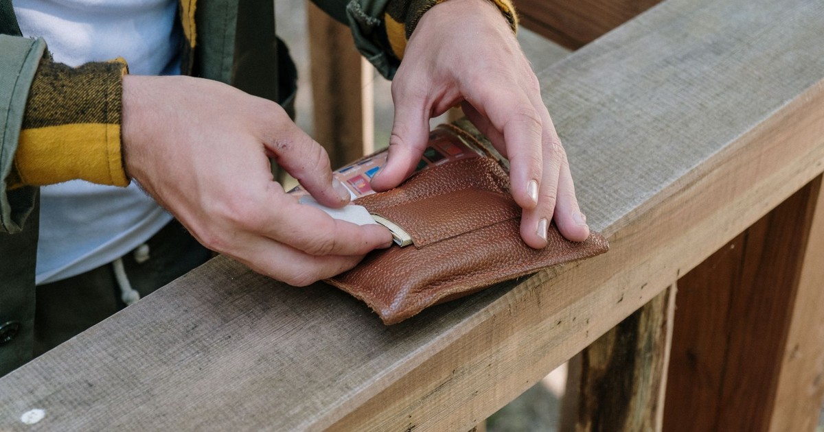 A man handling a leather wallet on a wooden railing, showcasing outdoor rustic style.