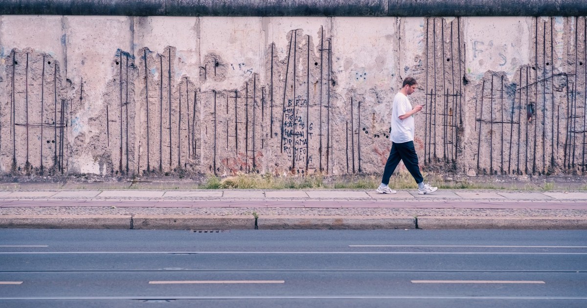 A person walks by the weathered Berlin Wall remnants, symbolizing history and change.