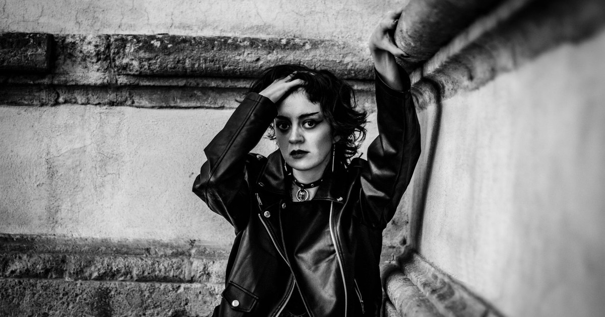 A striking monochrome portrait of a young adult in a leather jacket against a textured wall.