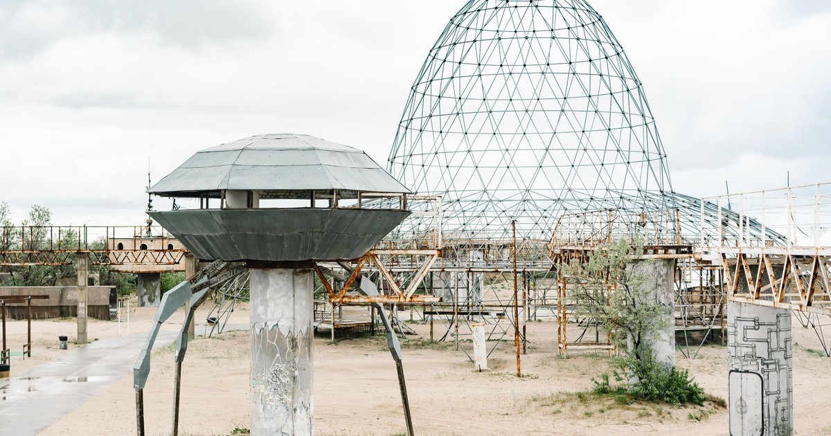 A metallic UFO-like structure in a deserted, sandy park under cloudy skies.