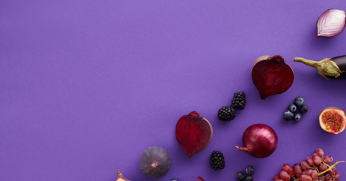Vibrant display of fresh fruits and vegetables on a purple background in a flat lay composition.