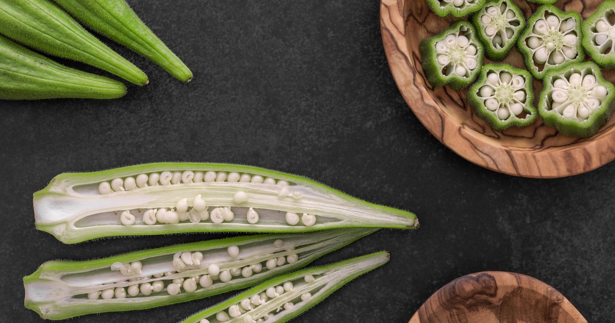 Close-up of fresh okra pods and slices on a dark background.