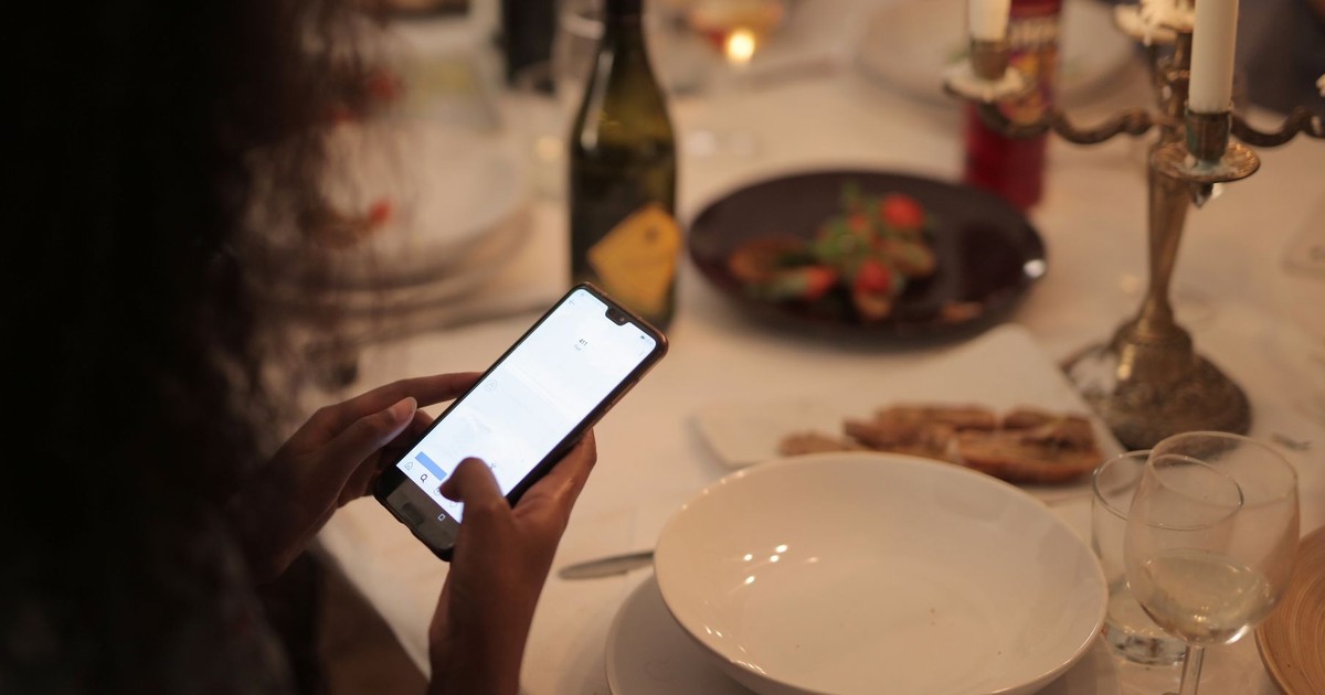 A cozy dinner setting with a woman using a smartphone at a candlelit table.