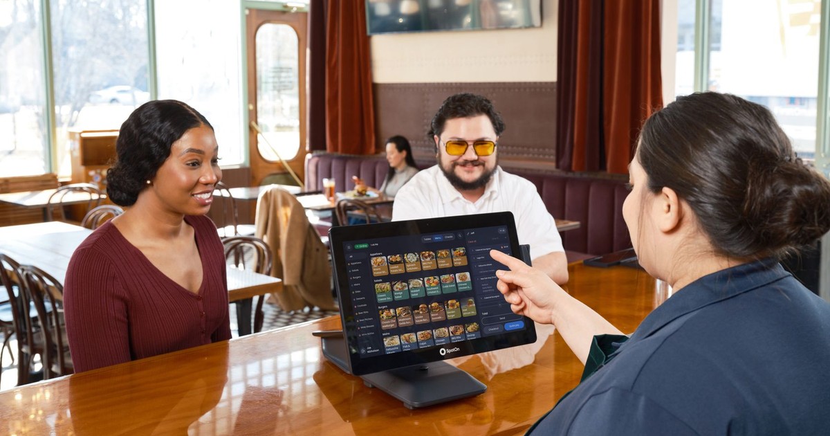 Server demonstrating a SpotOn POS system for customers in a cozy restaurant setting.