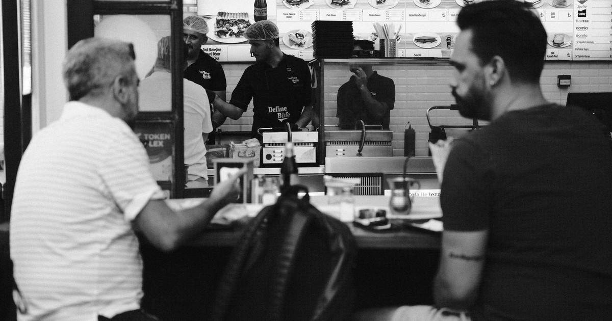 Monochrome photo of a fast food diner with customers and staff behind the counter.