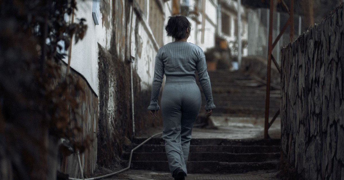 A woman in casual attire walks up concrete steps in a gritty urban environment, ideal for themes of solitude and determination.