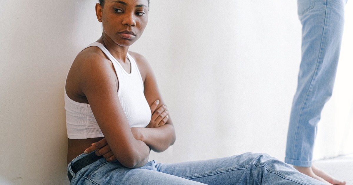 A woman sitting on the floor with crossed arms, expressing deep thought or disagreement.