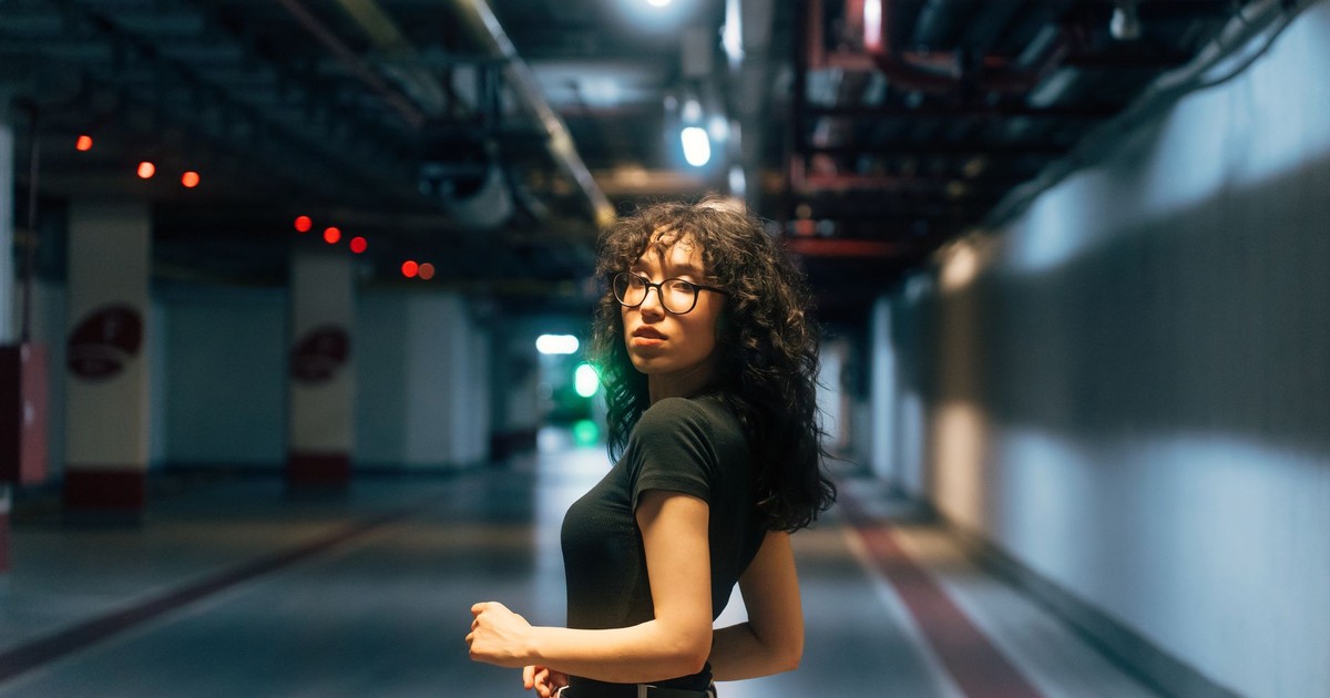 Fashionable woman with glasses in a moody underground location, vibrant lighting.