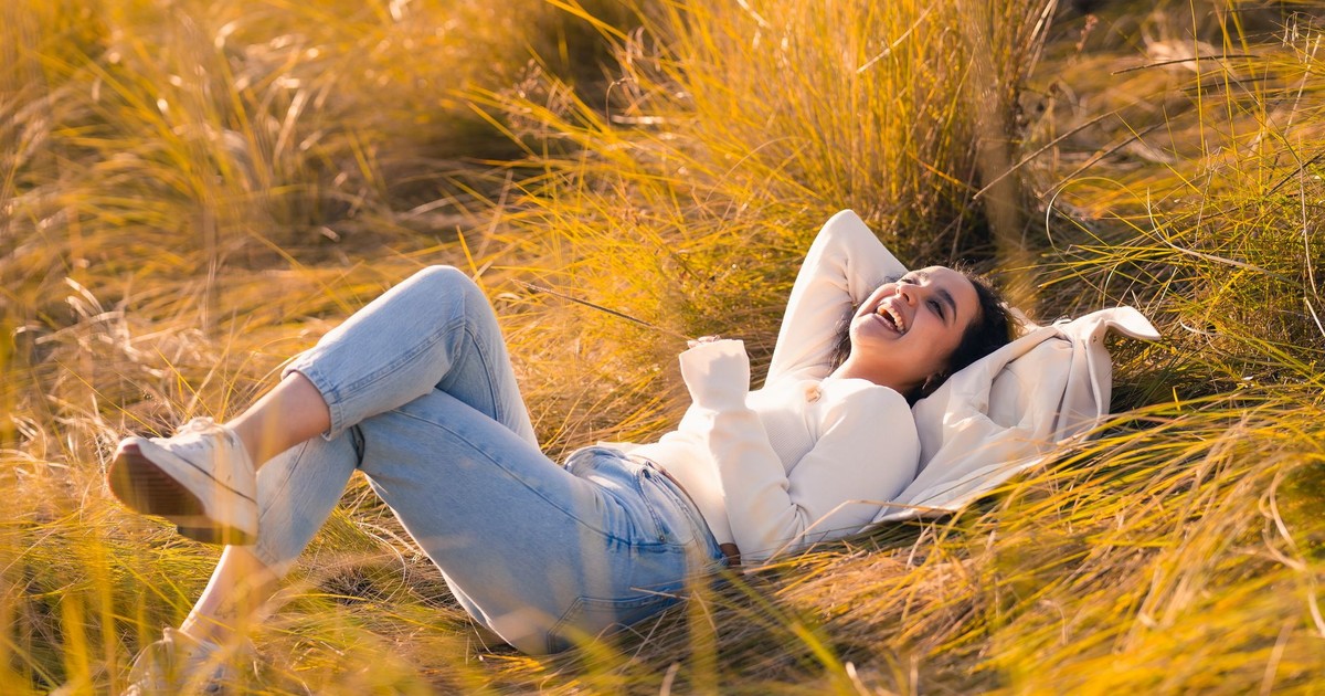 Young woman joyfully relaxing in a sunlit grassfield, embracing nature's beauty.