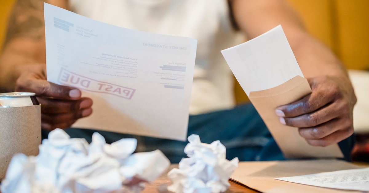Man sitting indoors reviewing past due bills with crumpled papers on a coffee table.